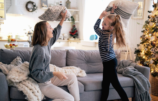 Mother and daughter playing pillow fight in sofa at home. Christmas morning, holidays, new year, soft colors. - Photo, image