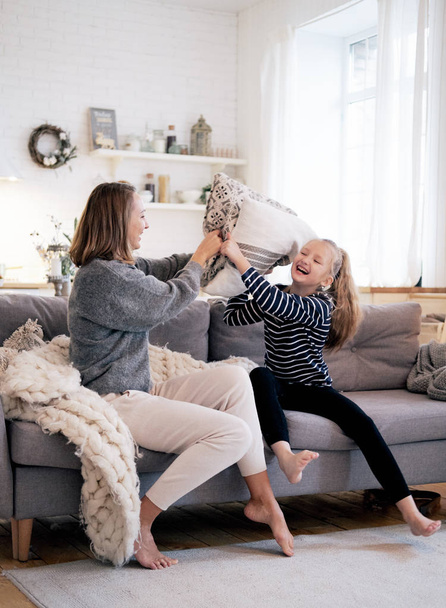 Mother and child having fun in pillow fight on sofa bed in bedroom. Happy family spending time together at home. - Fotoğraf, Görsel