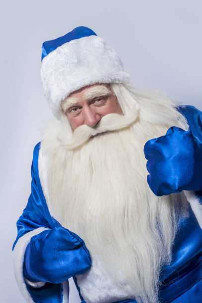 Weihnachtsmann und Väterchen Frost im blauen Mantel stehen vor einem isolierten weißen Hintergrund. ein Ältester ein Patriarch und ein Zauberer schaut auf jemanden oder etwas. - Foto, Bild