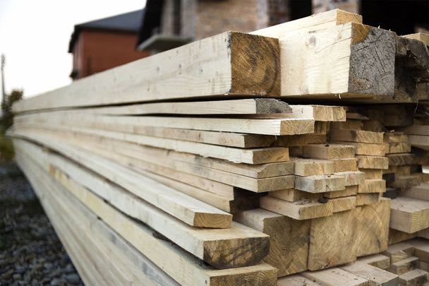 Auf der Baustelle stapeln sich naturbraune, unebene Holzbretter. Industrieholz für Zimmerei, Bau, Reparatur und Möbel, Bauholz für den Dachbau. - Foto, Bild