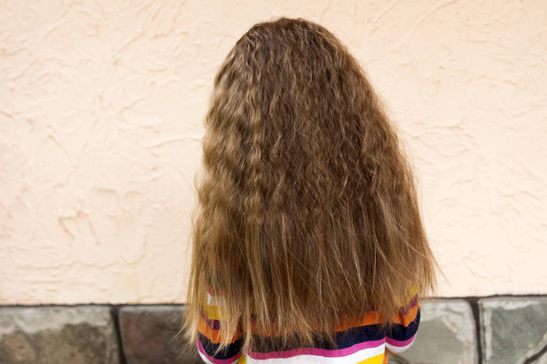 Rückseite der jungen Mädchenkopf mit langen blonden lockigen Haaren im Freien auf sonnigen Sommer weißen Stuck Wand kopieren Weltraum Hintergrund. Mode- und Friseurkonzept. - Foto, Bild