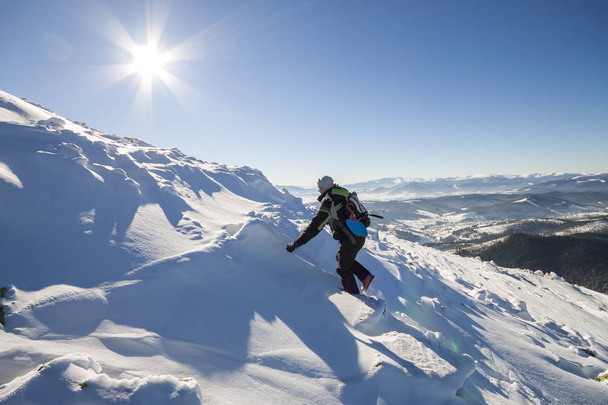 Turisztikai természetjáró mászó-a téli ruházat, hátizsák, hegymászó veszélyes sziklás meredek hegy lejtőjén hóval mély, fényes, ragyogó kék ég másol hely háttérben fehér nap sugarai. - Fotó, kép