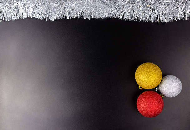 drei Christbaumkugeln liegen auf schwarzem Hintergrund mit wenig Licht und silbernem Lametta, Weihnachtsdekoration. - Foto, Bild