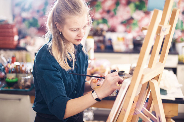 Young Woman Artist Working On Painting In Studio. Selective focus on foreground. - Valokuva, kuva