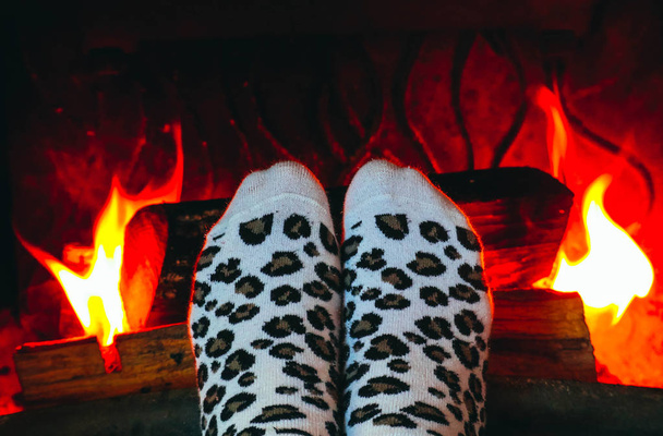 Verbranden van hout bij de open haard, vrouwelijke benen in sokken warming-up. Brandhout bakstenen op het vuur, vrouw voet Verwarming. - Foto, afbeelding