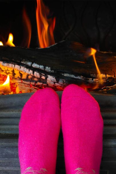 Verbranden van hout bij de open haard, vrouwelijke voeten in roze sokken warming-up. Brandhout bakstenen op het vuur, vrouw voet Verwarming. - Foto, afbeelding