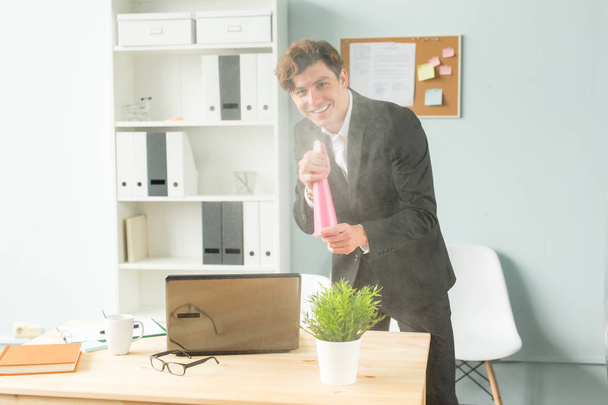 Office, humor, grap en zakelijke mensen concept - knappe man werkzaam in kantoor, drenken ingegoten plant - Foto, afbeelding