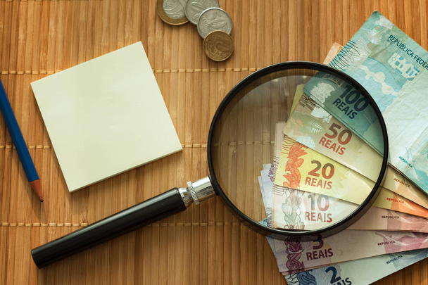 Brazilian money and magnifying glass and a notebook  - Φωτογραφία, εικόνα