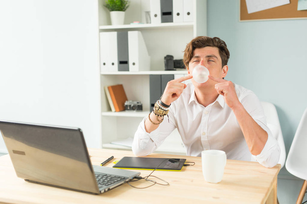 Geschäfts-, Spaß- und Witz-Konzept - Junger Mann pustet Kaugummi-Blase im Büro - Foto, Bild