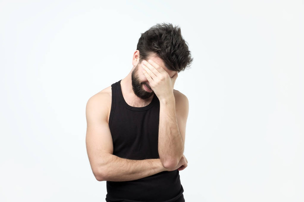 Young guy with a beard covers face with his hand and looks down. - Zdjęcie, obraz