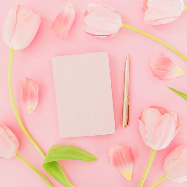 Kompozycja kwiatowa kwiatów tulipany z Notatnik i długopis na różowym tle. Widok płaski świeckich, top. Tło wiosna czas. - Zdjęcie, obraz