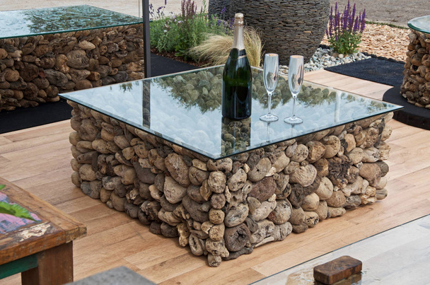 A coffee table made from driftwood with a modern glass top in a garden covered seating area - Photo, Image