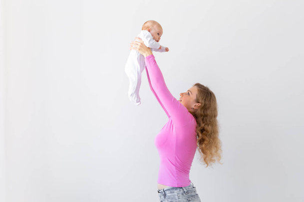 Motherhood, infant and people concept - mother throws baby up, laughing and playing with him on white background with copy space - Foto, imagen