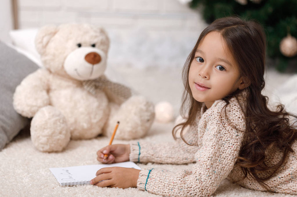 Χαριτωμένο παιδί κορίτσι, γράφει γράμμα στον Άγιο Βασίλη στο σπίτι - Φωτογραφία, εικόνα