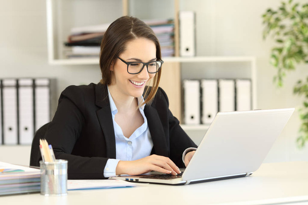 Happy office worker wearing eyeglasses working online writing in a laptop - Foto, immagini