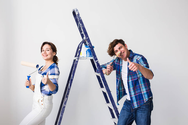Repair, renovation and love couple concept - young man and woman in love and painting the wall, showing thumbs up - Photo, Image