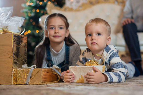 Little brother and sister with Christmas gifts lying on the floor - 写真・画像