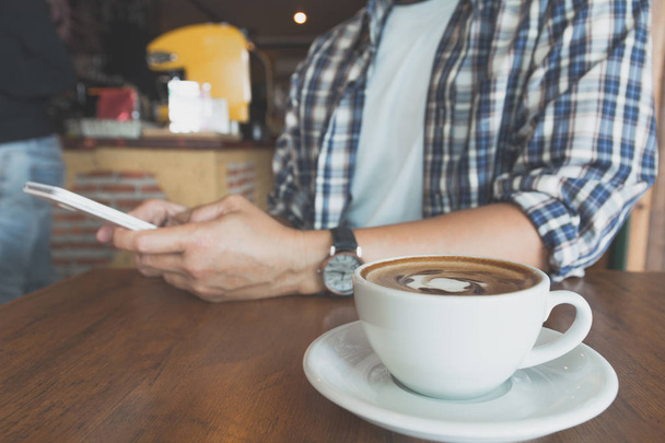 Чоловік використовує смартфон з чашкою кави на дерев'яному столі
. - Фото, зображення