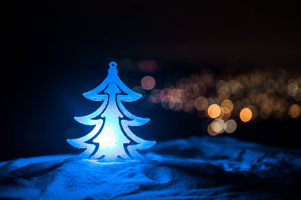 Decoraciones navideñas. Árbol de abeto de pie sobre la nieve con hermoso fondo decorado de vacaciones y atributos navideños tradicionales. Enfoque selectivo. Espacio vacío para tu texto
 - Foto, imagen
