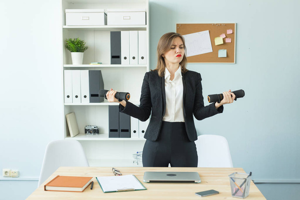Business, fitness in office and people concept - Satisfied woman in office holding dumbbell in hand - Фото, изображение