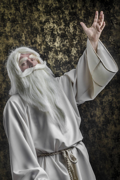 A grey-haired bearded severe wizard in a white cloak is doing magic against a magical dark-gold background. - Foto, imagen