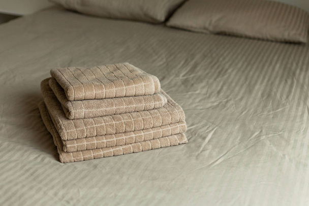 Stack of beige hotel towel on bed in bedroom interior. Soft focus. - Фото, зображення
