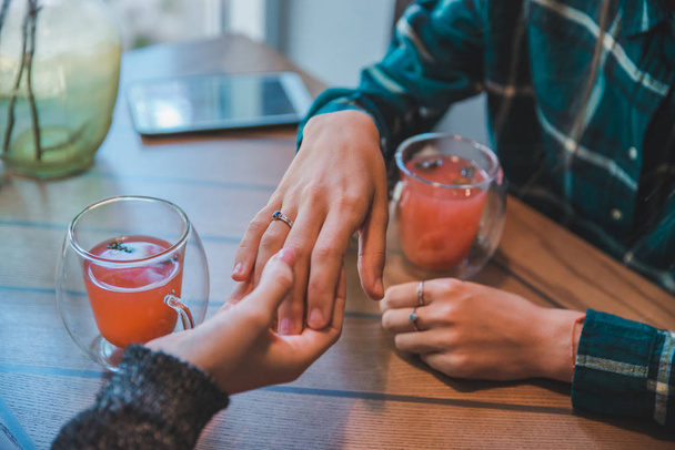 mujer muestra anillo de compromiso a amigo en la cafetería mientras bebe té de frutas caliente
 - Foto, Imagen