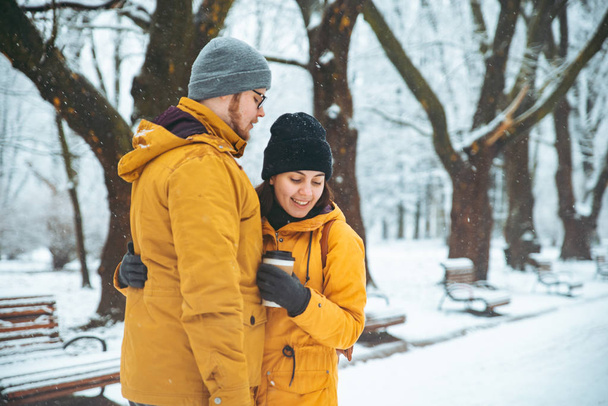 カップルは、冬雪が降った公園で抱っこ。行きコーヒーを飲んで寒い日コンセプトでウォーム アップする - 写真・画像