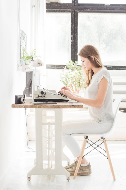 Young business woman working at home and typing on a typewriter. Creative Scandinavian style workspace - Fotó, kép