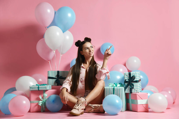A cute sexy dressed young woman sits on the floor among balloons and gift boxes. Concept of birthday, bachelorette party, wedding - 写真・画像