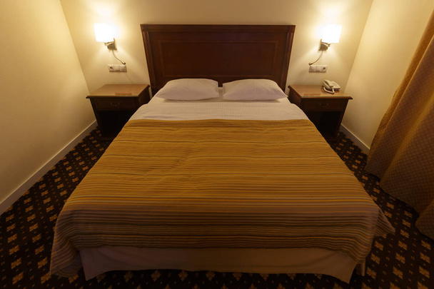 großes bequemes Doppelbett in einem kleinen Hotelzimmer - Foto, Bild