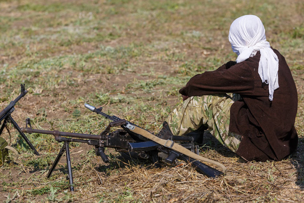 White veiled soldier sits on the ground close to a machine gun - Photo, Image