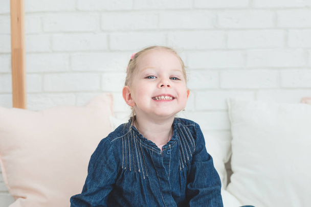 Cute little girl in blue denim overalls sitting on the bed. - Foto, Bild