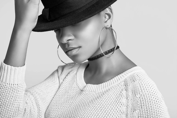 Detailní portrét mladé krásné bokové černé dívky v bílý svetr a módní klobouk izolovaných na bílém pozadí. Studio pro natáčení. - Fotografie, Obrázek