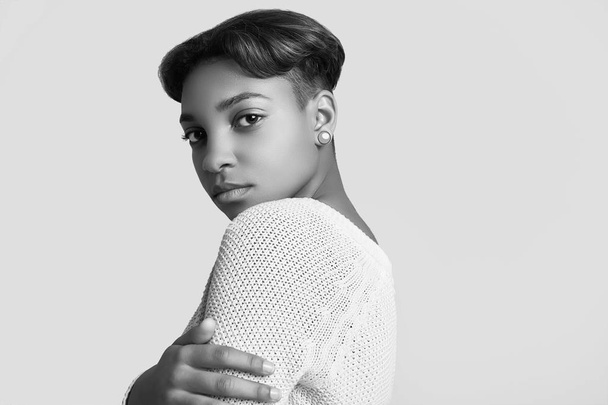 Close portrait of young beautiful hipster black girl with short hair in white sweater isolated on white background. Studio shoot. - Fotó, kép