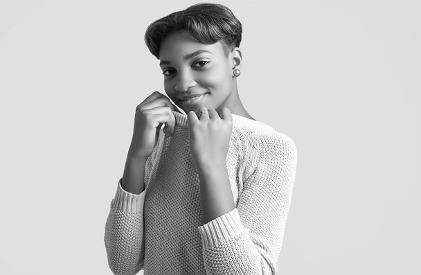 Retrato de joven hermosa chica negra hipster con el pelo corto sonriendo en suéter blanco aislado sobre fondo blanco. Sesión de estudio
. - Foto, Imagen