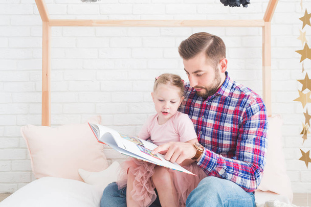 Dad and daughter sit together and read a book. - Zdjęcie, obraz