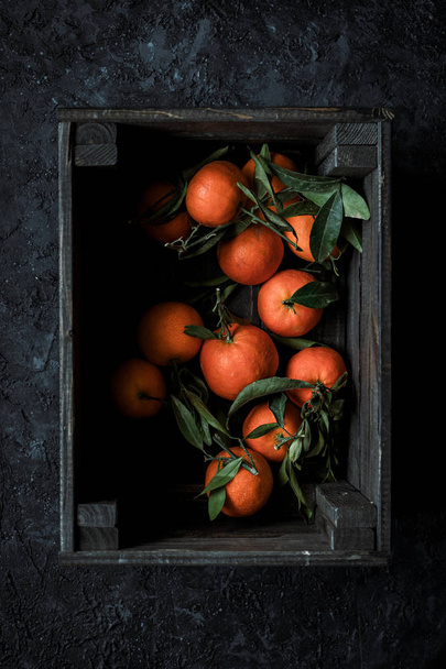 Récolte fraîche. mandarines mûres biologiques ou des oranges mandarines avec des feuilles dans une boîte en bois. Vue du dessus
 - Photo, image