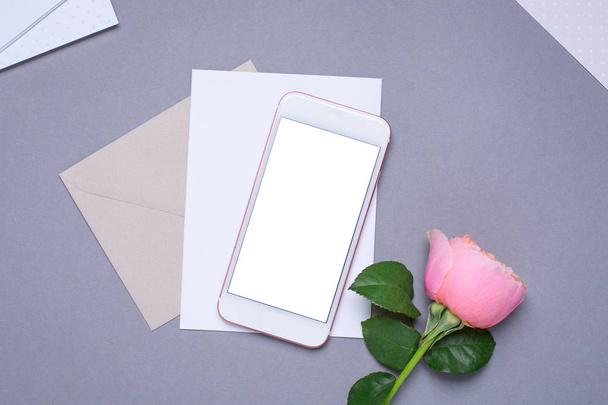 Handy und Umschlag mit rosa Rose auf grauem Hintergrund von oben - Foto, Bild