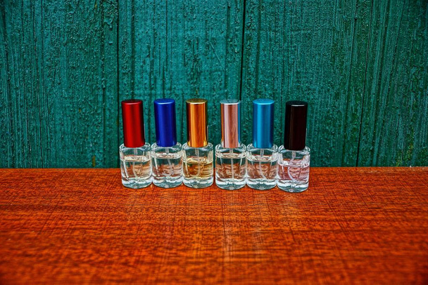 Joukko pieniä värillisiä pulloja, joissa on hajuvettä pöydällä lähellä puuseinää
 - Valokuva, kuva