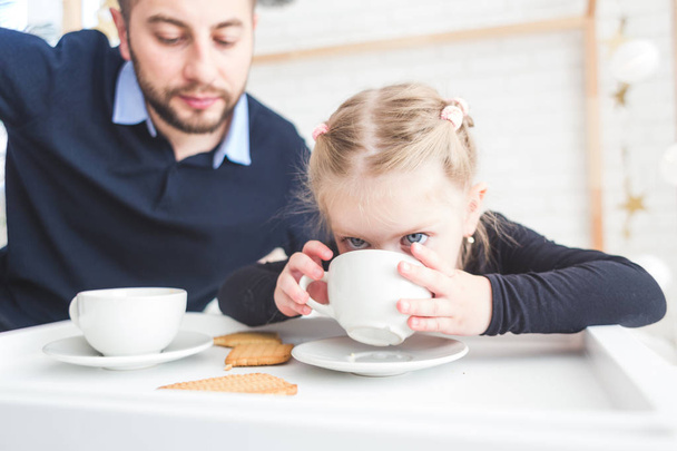 Cute little girl and her father drink tea with cookies at home. - Foto, Imagen