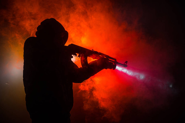 Silhouette of man with assault rifle ready to attack on dark toned foggy background or dangerous bandit holding gun in hand. Shooting terrorist with weapon theme decor - 写真・画像