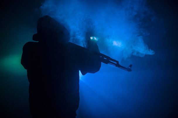 Silhouette of man with assault rifle ready to attack on dark toned foggy background or dangerous bandit holding gun in hand. Shooting terrorist with weapon theme decor - Photo, Image