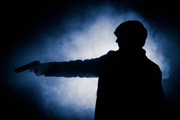 Silhouet van man met pistool klaar om te vallen op donker getinte mistige achtergrond of gevaarlijke bandit bedrijf pistool in de hand. Schieten terrorist met wapen thema inrichting - Foto, afbeelding