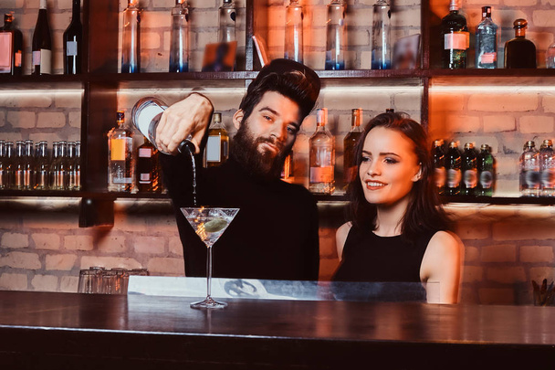 Parrakas baarimikko, jolla on itsevarma ilme, tekee cocktailin kauniin tytön kanssa tiskin takana
 - Valokuva, kuva