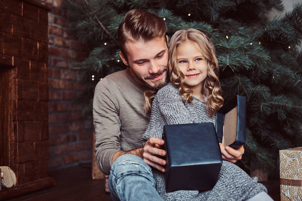 Liebe, Familie, Vaterschaft, Weihnachten. Glücklicher Vater und seine süße kleine Tochter öffnen Geschenke, während sie auf dem Boden sitzen - Foto, Bild
