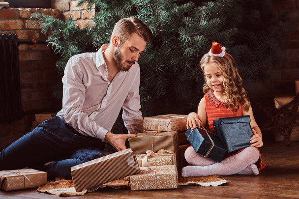 Батько і дочка, сидячи на підлоги оточенні подарунки поруч з будинку ялинку.  - Фото, зображення