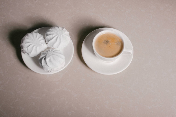 Een kopje verse koffie, americano en drie heerlijk zoete dessert witte marshmallows op een schotel close-up. Kopiëren van ruimte - Foto, afbeelding