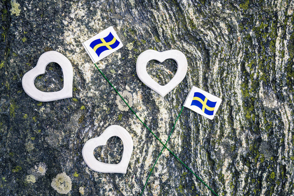 Σουηδική σημαίες και άσπρο ξύλινες καρδιές σε ποώδη ροκ υπόβαθρο. Σκανδιναβική φύση. - Φωτογραφία, εικόνα