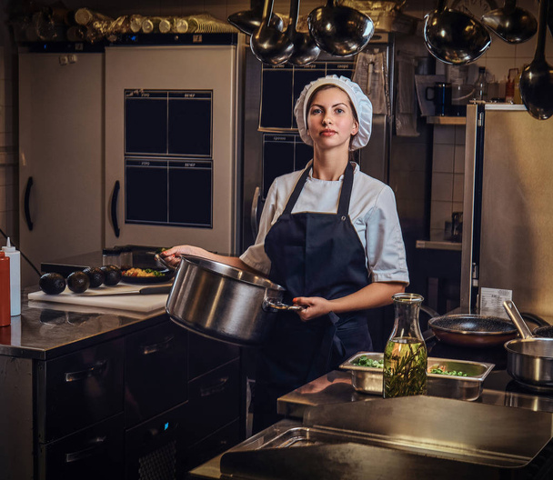 Female chef wearing a uniform holding a pan at restaurants kitchen. - Фото, зображення